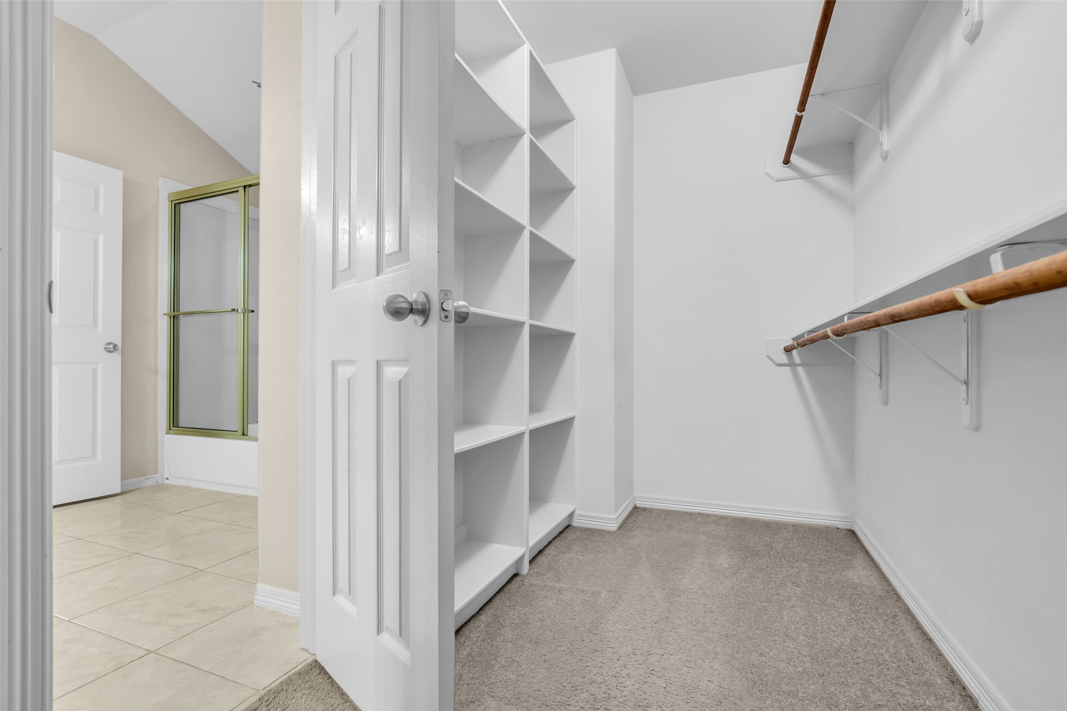 1898 Longmire Road, Unit 5 Conroe, TX 77304 - Photo 33 of 48 This photo showcases a spacious walk-in closet with ample shelving and hanging space. It features carpeted flooring and is adjacent to a bathroom with tiled flooring and a glass shower door.