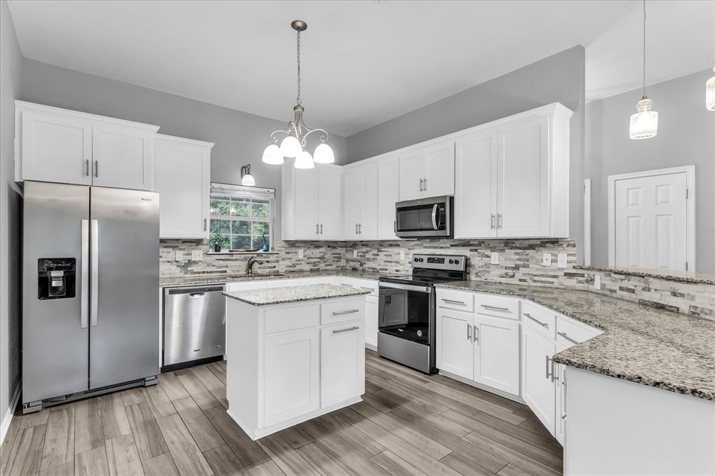 7 Market Loop Morgan's Point Resort, TX 76513 - Photo 6 of 31 Open-concept kitchen featuring white cabinetry, stainless steel appliances, a multi-tone tile backsplash, light speckled countertops, and wood-finish flooring