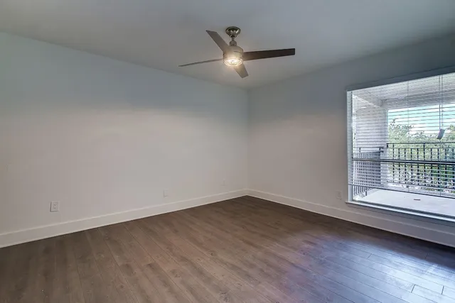 an empty room with wooden floor a ceiling fan and windows