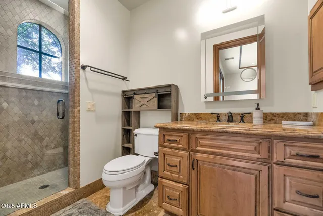 a bathroom with a toilet a sink a glass door a shower a mirror a vanity and window