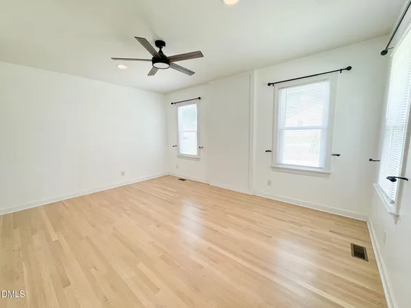 a view of empty room with wooden floor and fan