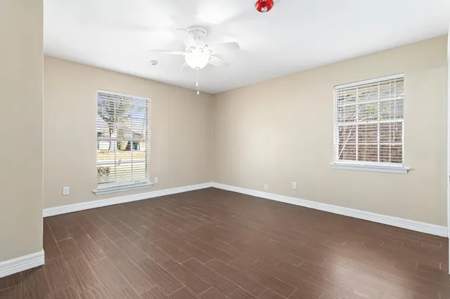 an empty room with wooden floor chandelier fan and windows