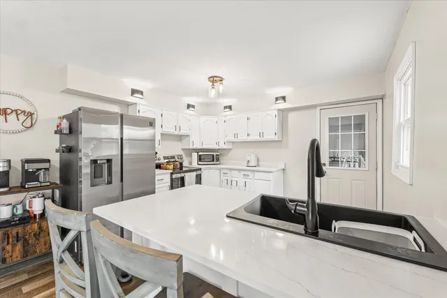 a kitchen with stainless steel appliances kitchen island granite countertop a refrigerator a stove and white cabinets with wooden floor