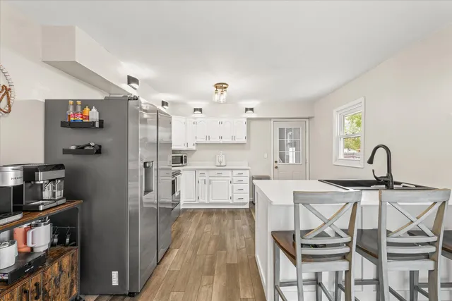 a kitchen with stainless steel appliances a refrigerator a stove a sink dishwasher and white cabinets with wooden floor