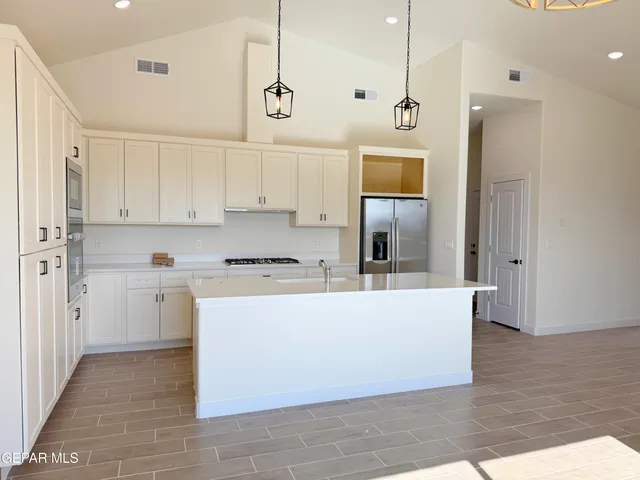 a living room with stainless steel appliances kitchen island granite countertop a refrigerator a stove a sink and white cabinets with wooden floor