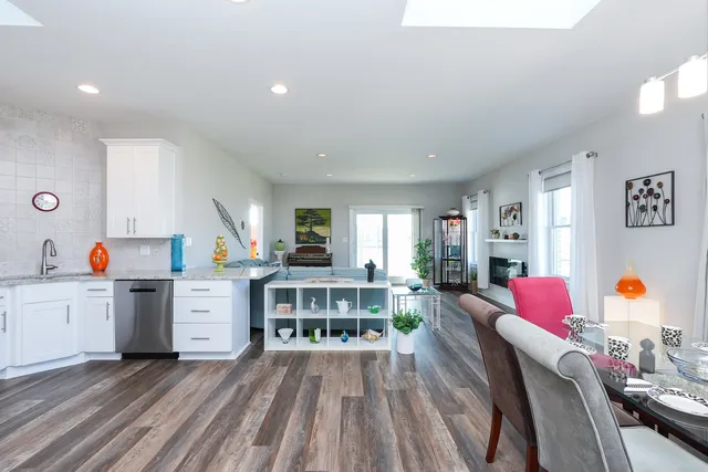 a living room with stainless steel appliances furniture wooden floor and a kitchen view