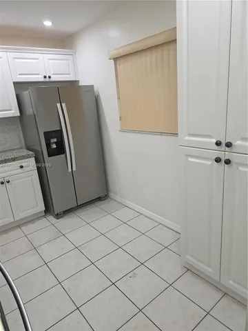 a view of kitchen with refrigerator and white cabinets