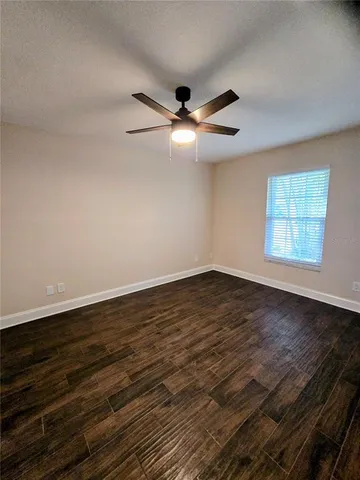 an empty room with wooden floor fan and windows