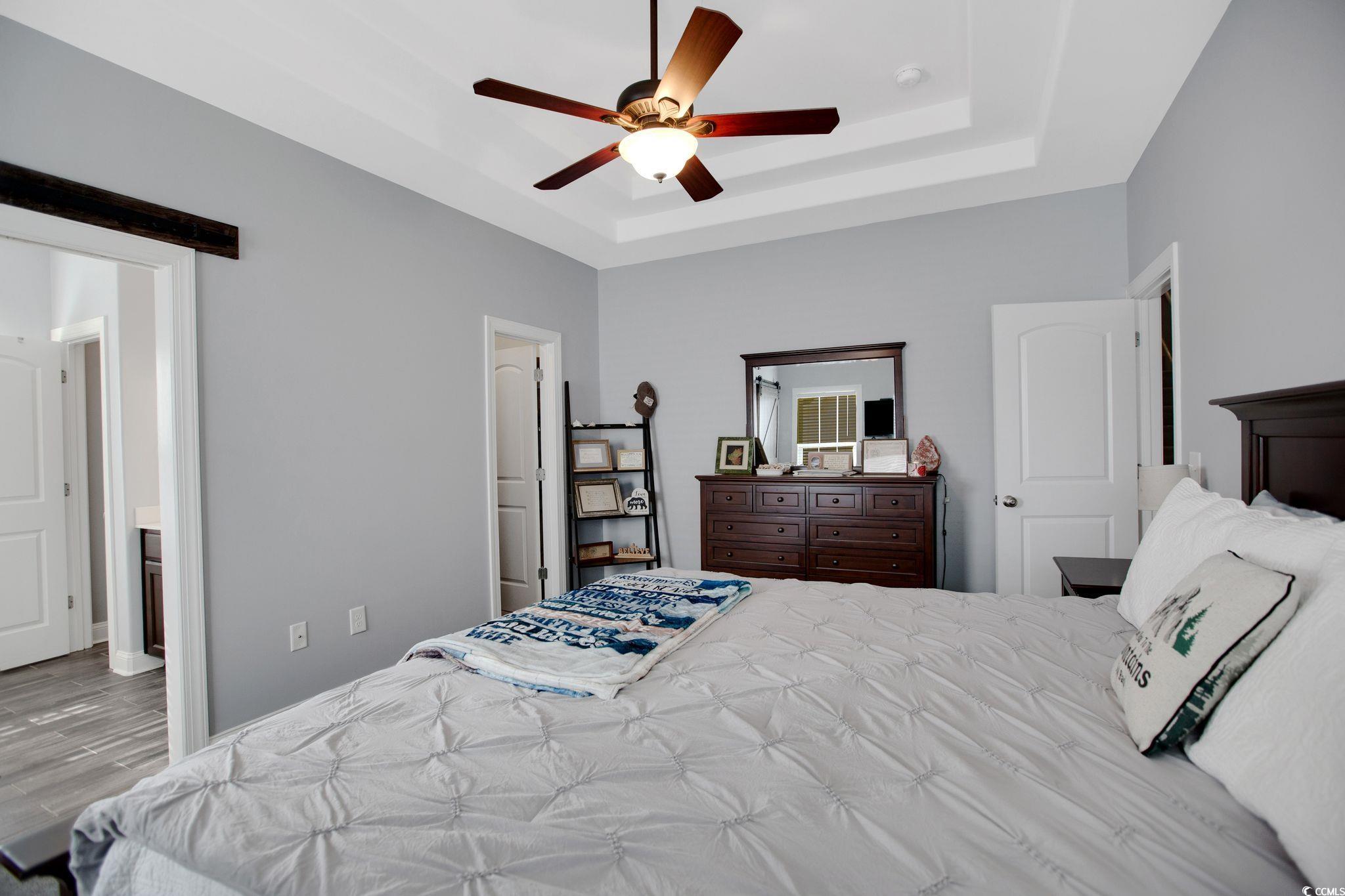 607 Garden Avenue Georgetown, SC 29440 - Photo 16 of 35 Bedroom with ceiling fan, a barn door, light wood-type flooring, and a tray ceiling