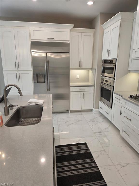 16370 Viansa Way, Unit 6 Naples, FL 34110 - Photo 16 of 27 Kitchen with white cabinets, stainless steel appliances, light marble finish floors, recessed lighting, and light stone countertops