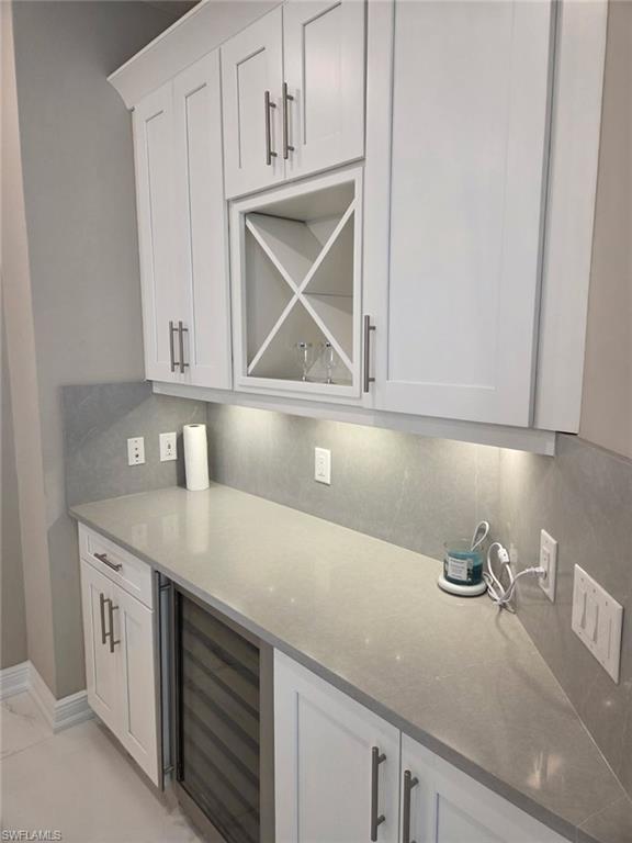 16370 Viansa Way, Unit 6 Naples, FL 34110 - Photo 4 of 27 Bar area with white cabinetry, light stone counters, beverage cooler, and decorative backsplash