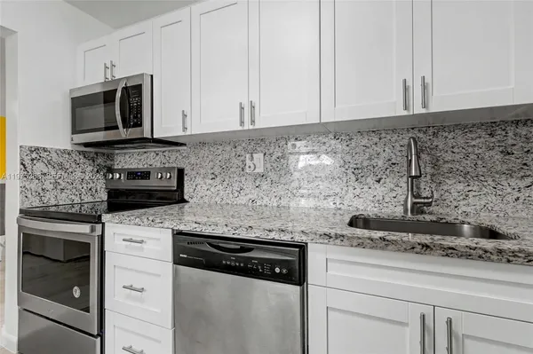a kitchen with granite countertop white cabinets and stainless steel appliances