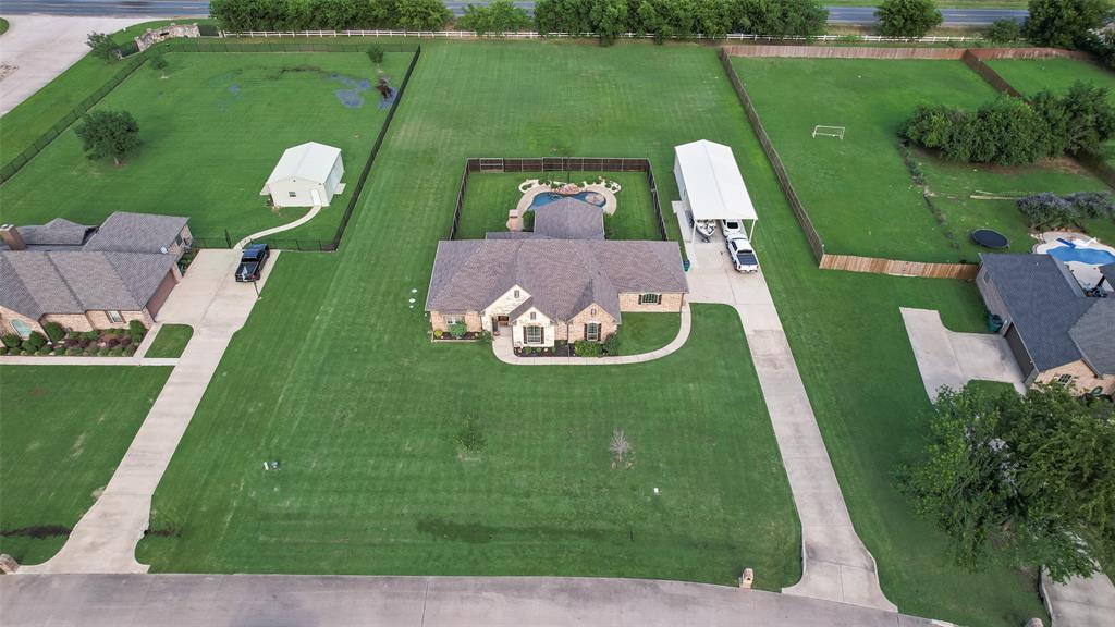 1132 Chartres Street Kaufman, TX 75142 - Photo 22 of 25 Expansive property featuring a brick exterior home, large green lawns, a detached two-car garage, a covered parking structure, and a fenced swimming pool area