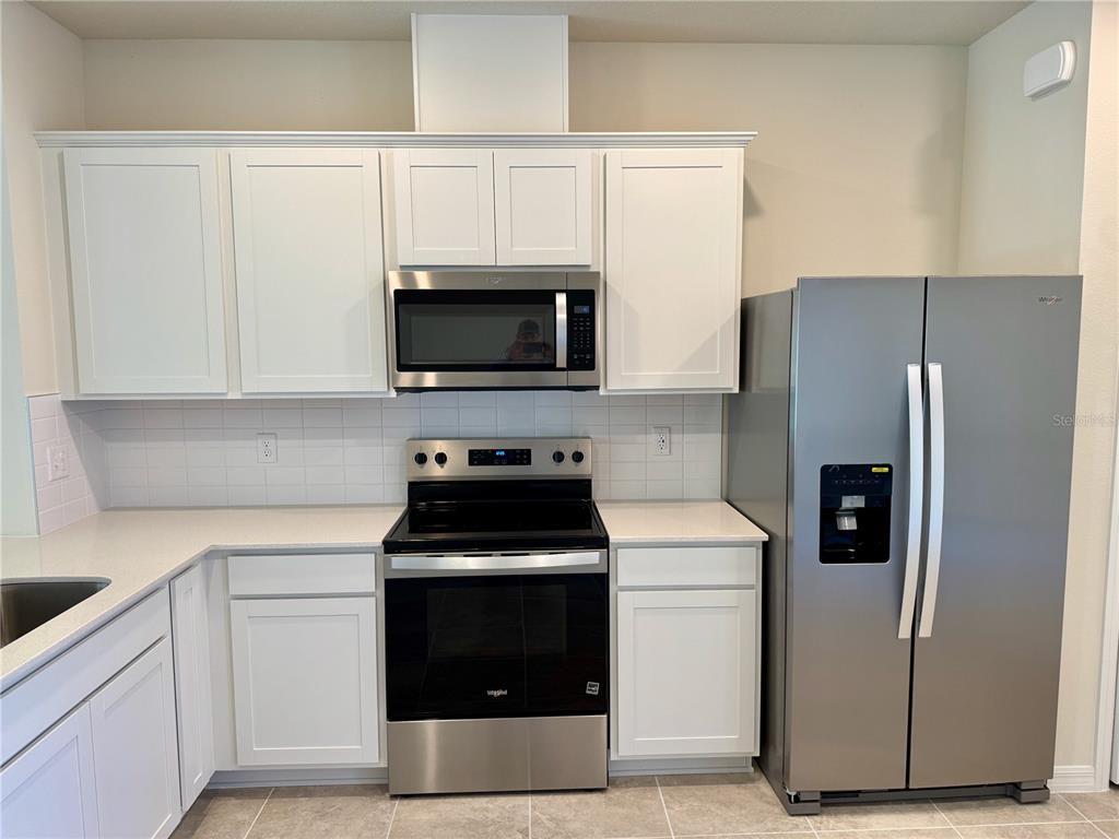 3059 Emerald Acrs Lane Sanford, FL 32771 - Photo 6 of 24 a kitchen with a refrigerator stove and white cabinets