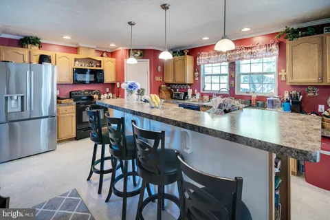 a kitchen with stainless steel appliances kitchen island granite countertop a dining table chairs sink refrigerator and microwave