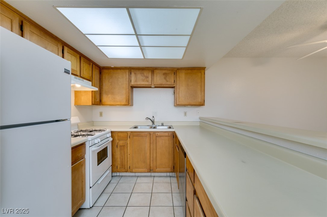 2681 Ruthe Duarte Avenue Las Vegas, NV 89121 - Photo 25 of 43 Kitchen featuring white appliances, under cabinet range hood, light tile patterned flooring, light countertops, and a sink