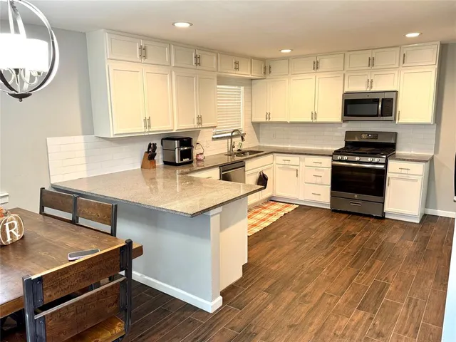 a kitchen with stainless steel appliances a stove a sink dishwasher a refrigerator white cabinets and wooden floor