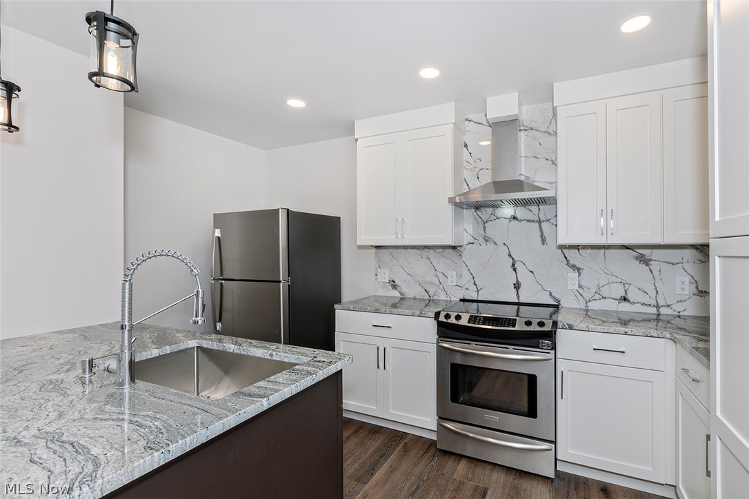 20601 Shelburne Road Shaker Heights, OH 44122 - Photo 25 of 29 First level Kitchen featuring appliances with stainless steel finishes, light stone counters, dark wood-type flooring, wall chimney exhaust hood, and decorative backsplash