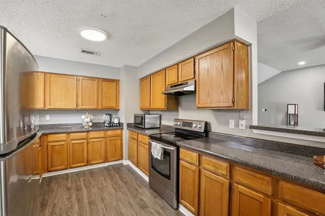 a kitchen with stainless steel appliances granite countertop wooden cabinets a sink a stove a refrigerator with grey cabinets and wooden floor