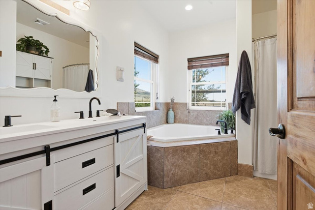 1634 West Arimo Road Arimo, ID 83214 - Photo 20 of 89 Bathroom featuring a double vanity with barn door style cabinetry, matte black fixtures, a built-in corner soaking tub with tile surround, and tile flooring