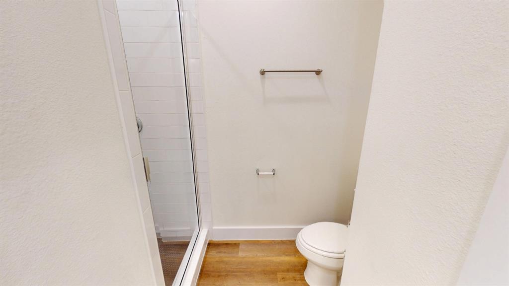 313 Buck Ridge Drive Frisco, TX 75068 - Photo 19 of 20 Bathroom featuring a glass-enclosed shower with subway tile surround, a standard toilet, wood-finish flooring, and brushed bronze fixtures