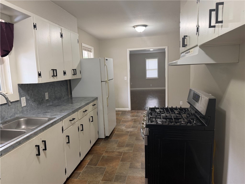 909 Riddell Street Clarksville, AR 72830 - Photo 8 of 26 Kitchen featuring white cabinetry with black hardware, a double basin stainless steel sink, and a black gas range with an overhead range hood