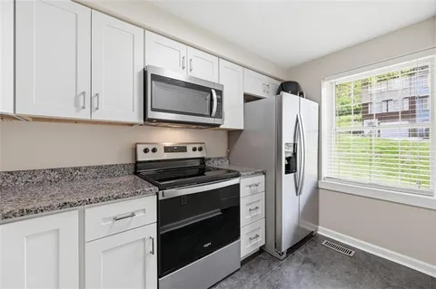a kitchen with stainless steel appliances granite countertop white cabinets and a window