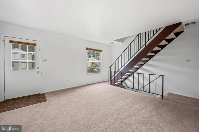 a view of an empty room with stairs and a living room