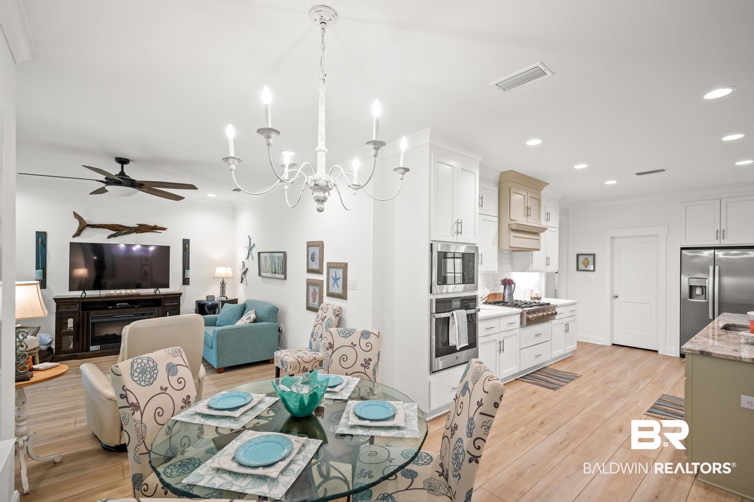 4601 Surrey Lane Orange Beach, AL 36561 - Photo 17 of 43 Dining space with ceiling fan with notable chandelier, a fireplace, and light hardwood / wood-style flooring
