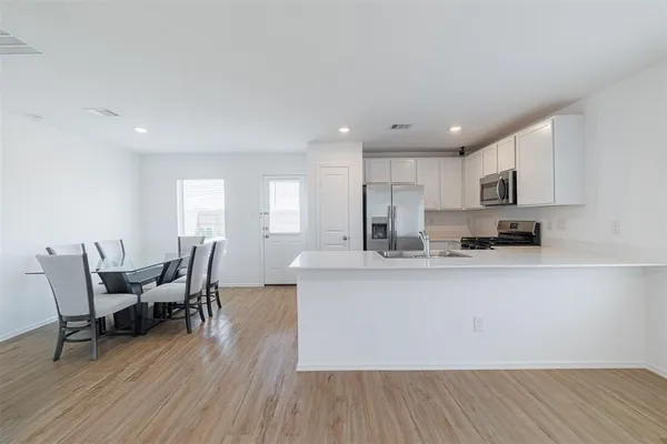 a large white kitchen with stainless steel appliances granite countertop a stove a sink a dining table and chairs