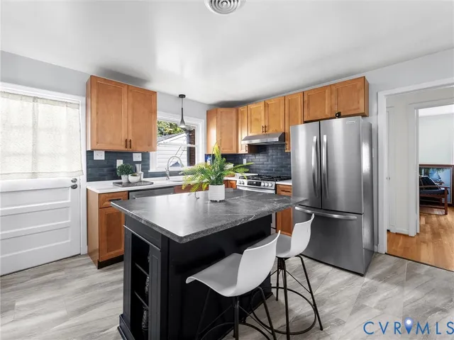 a kitchen with stainless steel appliances granite countertop a refrigerator a stove a sink and white cabinets with wooden floor