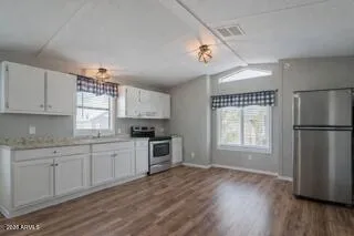 a kitchen with granite countertop a refrigerator a sink dishwasher a stove and white cabinets with wooden floor