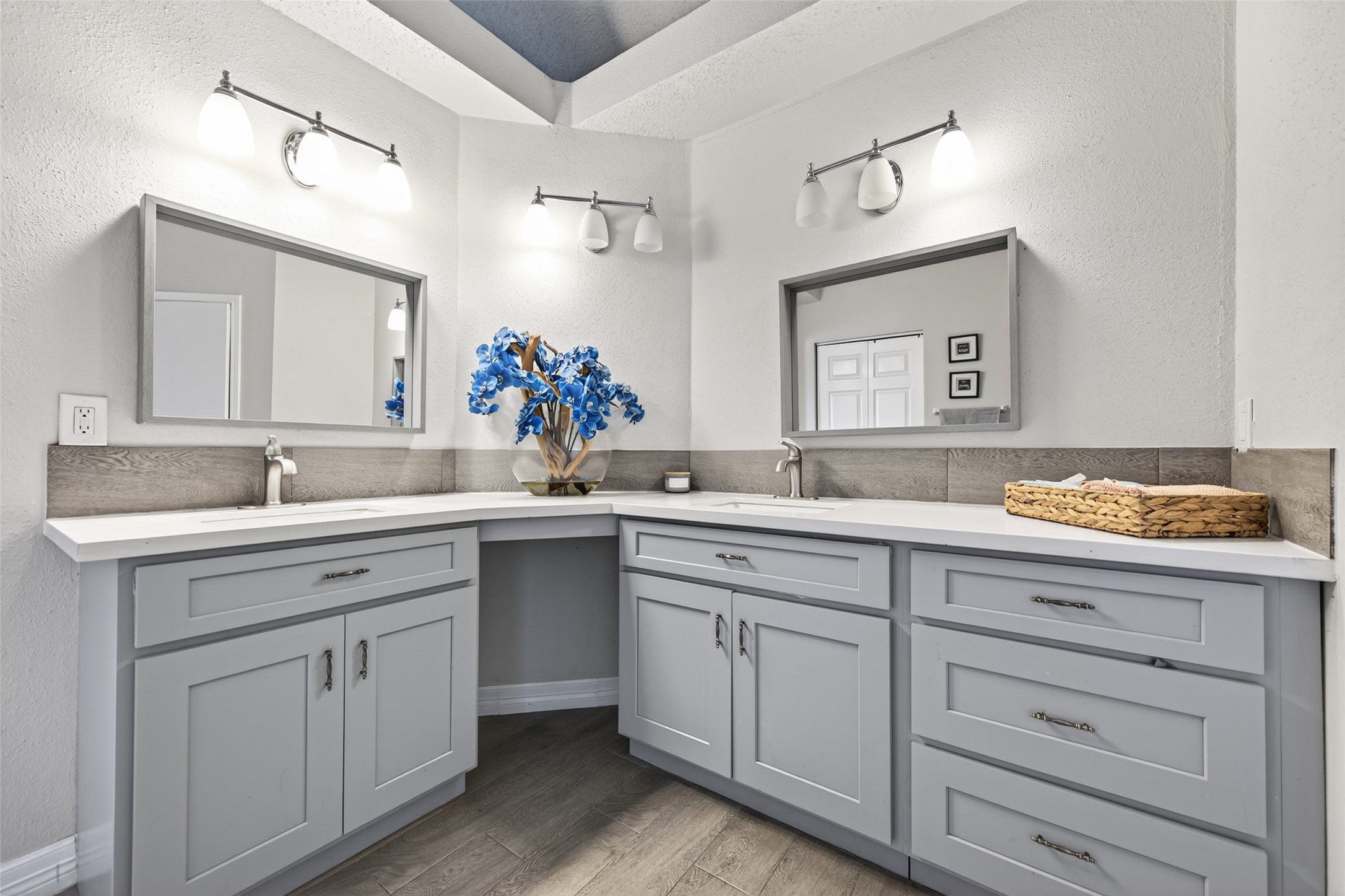 18446 North Willow Bluff Road Katy, TX 77449 - Photo 22 of 33 This bathroom features a dual-sink vanity with elegant gray cabinetry, modern fixtures, and bright lighting. The space is enhanced by decorative blue flowers and a clean, spacious countertop.