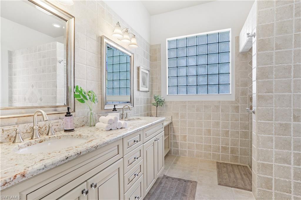 7699 Groves Road Naples, FL 34109 - Photo 20 of 30 a bathroom with a granite countertop sink a mirror and a shower