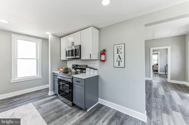 a kitchen with stainless steel appliances a stove a sink a refrigerator white cabinets and wooden floor