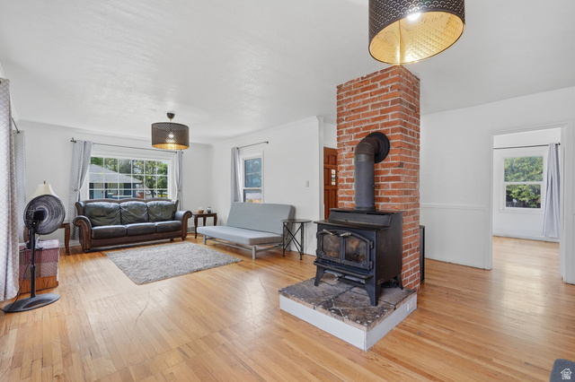 707 East 150 South Provo, UT 84606 - Photo 7 of 31 Living area featuring wood-finish flooring, a prominent brick column, and a black wood-burning stove with a stone hearth