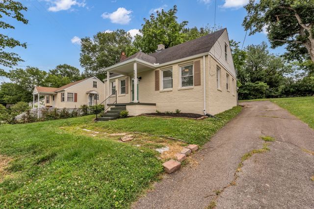 a white house with a small yard plants and large trees