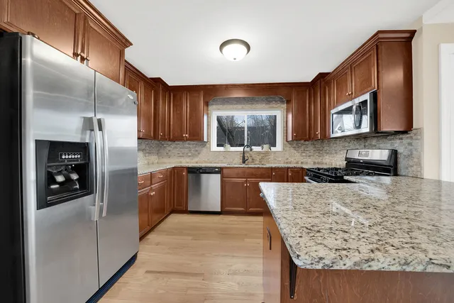 a large kitchen with stainless steel appliances granite countertop a refrigerator a stove and a sink with wooden cabinets