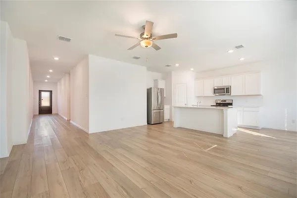 a view of an empty room and kitchen view with wooden floor