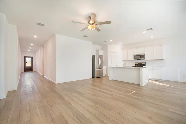 a view of an empty room and kitchen view with wooden floor