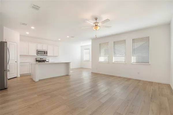 a view of an empty room with kitchen and window