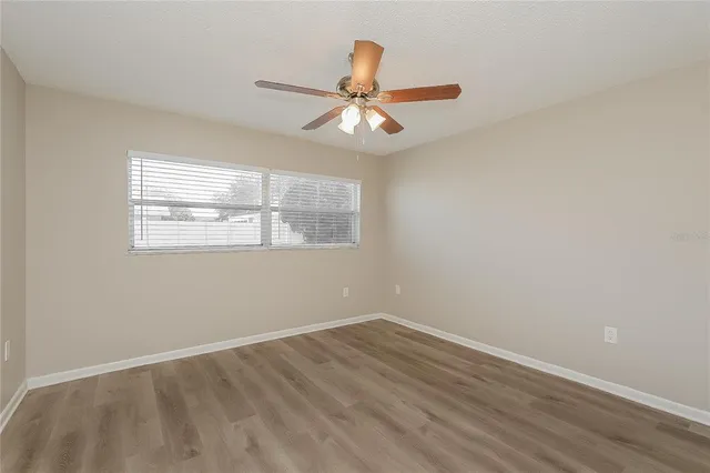 an empty room with wooden floor fan and windows