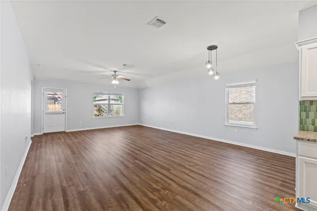 an empty room with wooden floor chandelier and windows