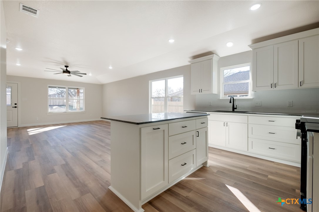 1208 Mill Street Gatesville, TX 76528 - Photo 9 of 28 a kitchen with granite countertop white cabinets white appliances with a sink and dishwasher with wooden floor