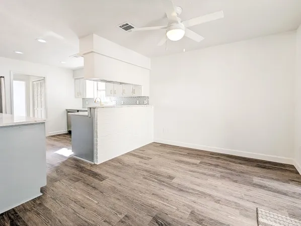an empty room with wooden floor fan and windows