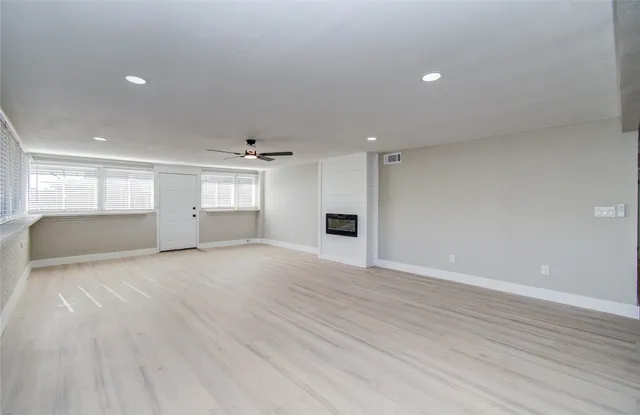 an empty room with wooden floor kitchen view and windows