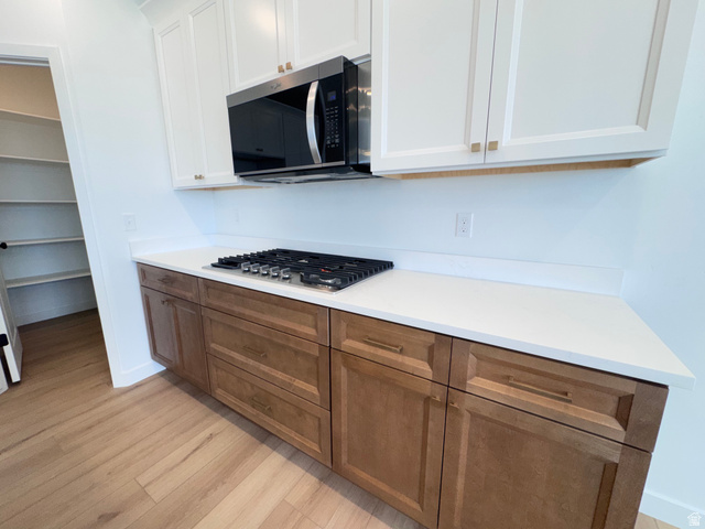 2613 Scarlet Road, Unit 258 Eagle Mountain, UT 84005 - Photo 12 of 33 Kitchen featuring a gas cooktop, built-in microwave, white upper cabinetry, wood-finish lower cabinetry, and light countertops