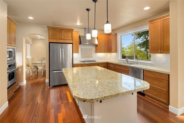 a kitchen with stainless steel appliances granite countertop a sink a refrigerator and a wooden floor