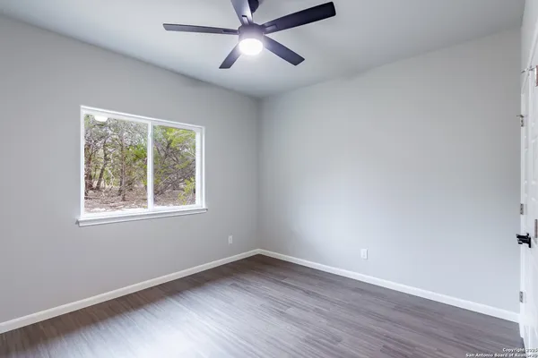 an empty room with wooden floor fan and windows