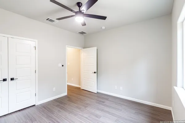 an empty room with wooden floor fan and windows